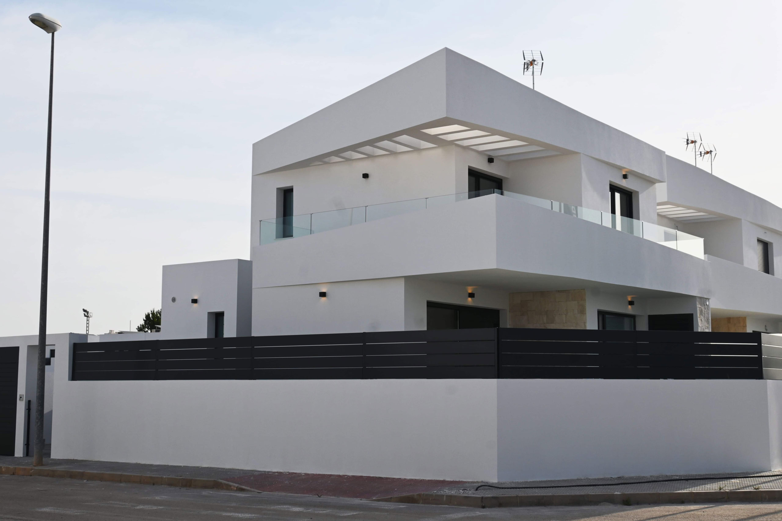 Moderne witte woning met ruime balkon en glazen balustrades, gelegen in rustige buurt.