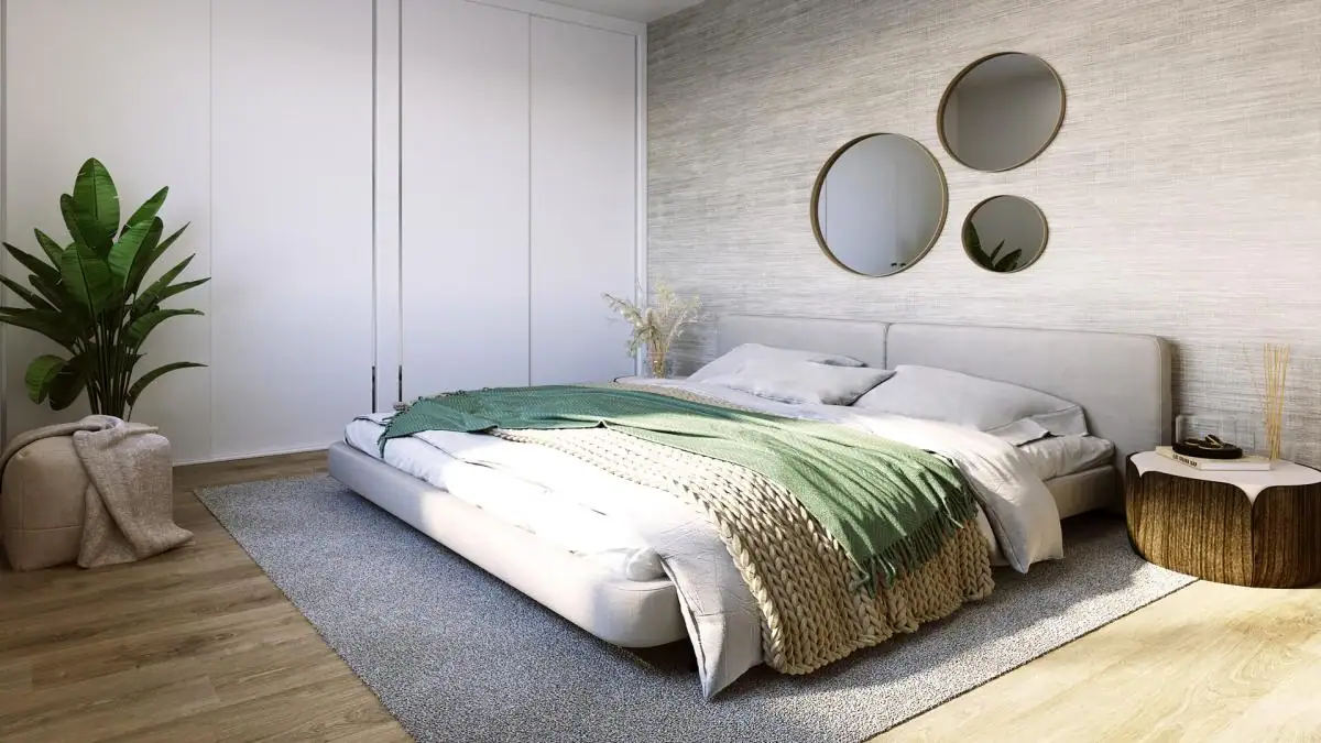 Ruime slaapkamer met wit bed, groene dekens en ronde spiegels aan de muur.