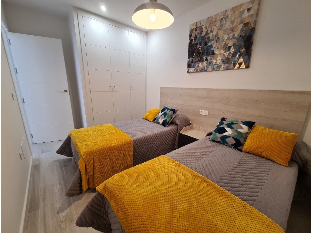 Moderne slaapkamer met twee eenpersoonsbedden, kleurrijke kussens en decoratief kunstwerk boven het.