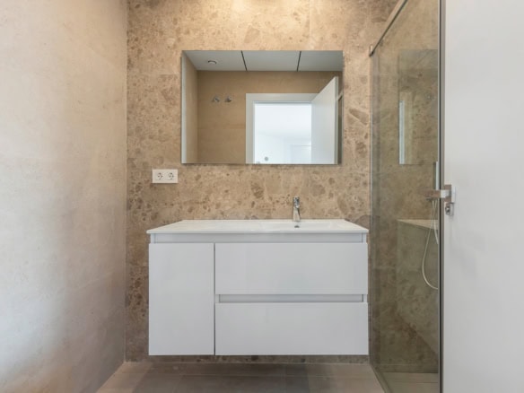Moderne badkamer met beige natuursteen muren en een witte wastafel onder spiegel.